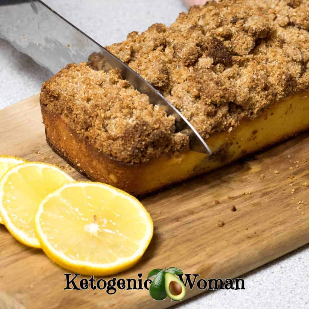 Keto Lemon Blueberry Coffee Cake on a wooden board with knife slicing through it.