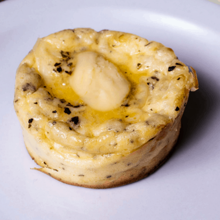 single cream cheese muffin with pat of butter on white plate